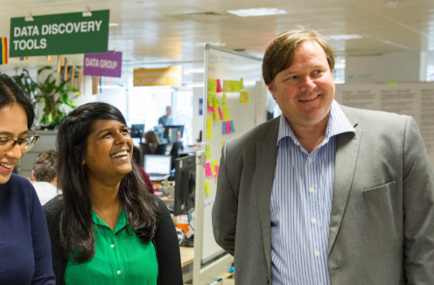 Simon Daly, Digital, Data and Technology Fast Streamer, standing with his colleagues in an office and smiling. In the background, there is a sign that reads "Data Discovery Tools"