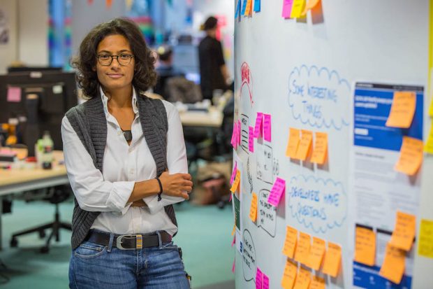 Fajer Qasem, Product manager, standing in an office next to the colourful post-it note wall