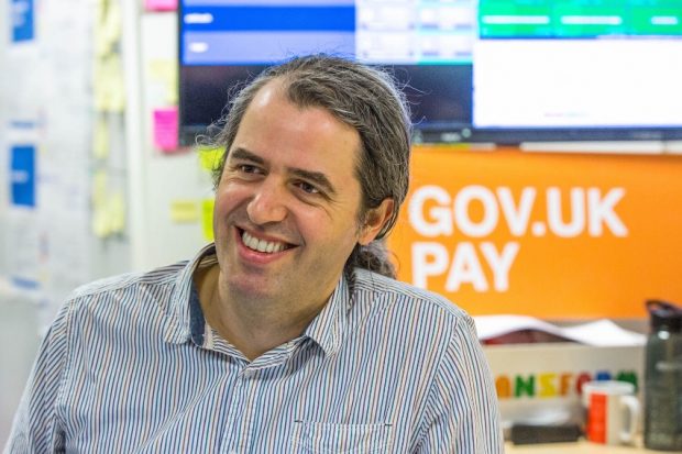 David Heath, smiling in the office next to a sign of "GOV.UK Pay"