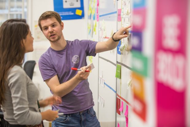 Thomas Fast Streamer, talking to a colleague next to a post-it notes wall