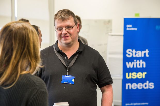 Mark Crombie talking to a colleague. There's a banner behind him saying "Start with user needs".