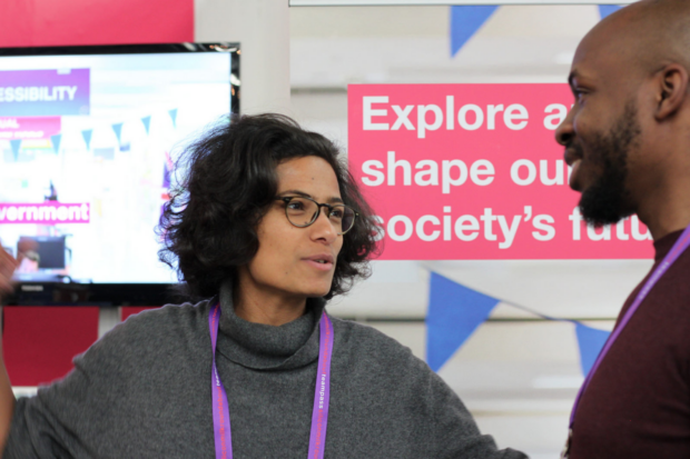 An image of two colleagues talking. There's a banner behind reading "Explore and shape our society's future"