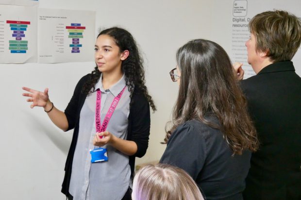 A woman wearing a Government Digital Service lanyard presents workforce data to an audience of government colleagues