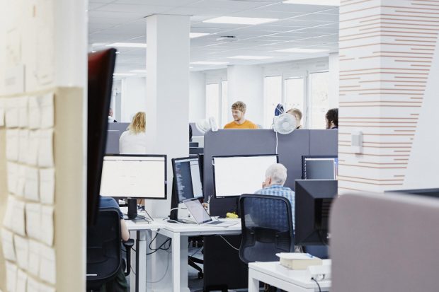 Office work environment, with people working at computers and talking to each other