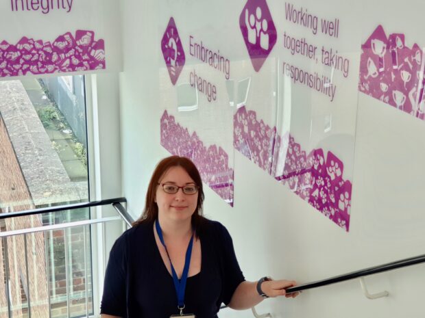 Blog post author standing in the staircase, facing the camera. The walls have purple writings on them with sayings "Working well together, taking responsibility" and "Embracing change"