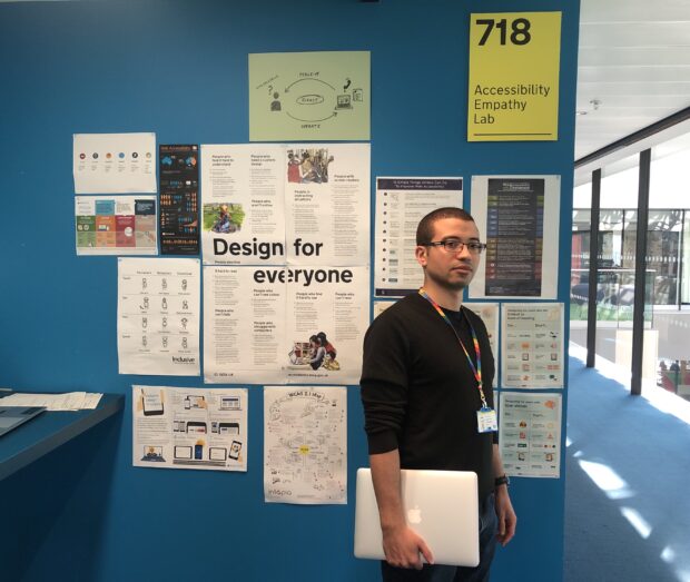 Jonathan Glassman stands in front of a wall covered with posters. One of these reads "Design for everyone".