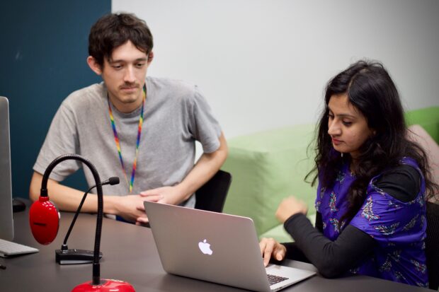 A male user researcher is listening to a presentation from a female client.