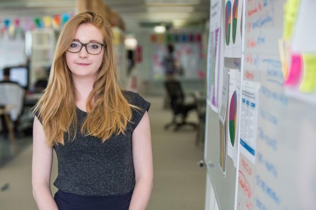 Jen Lambourne standing next to a wall covered with posters showing charts and diagrams