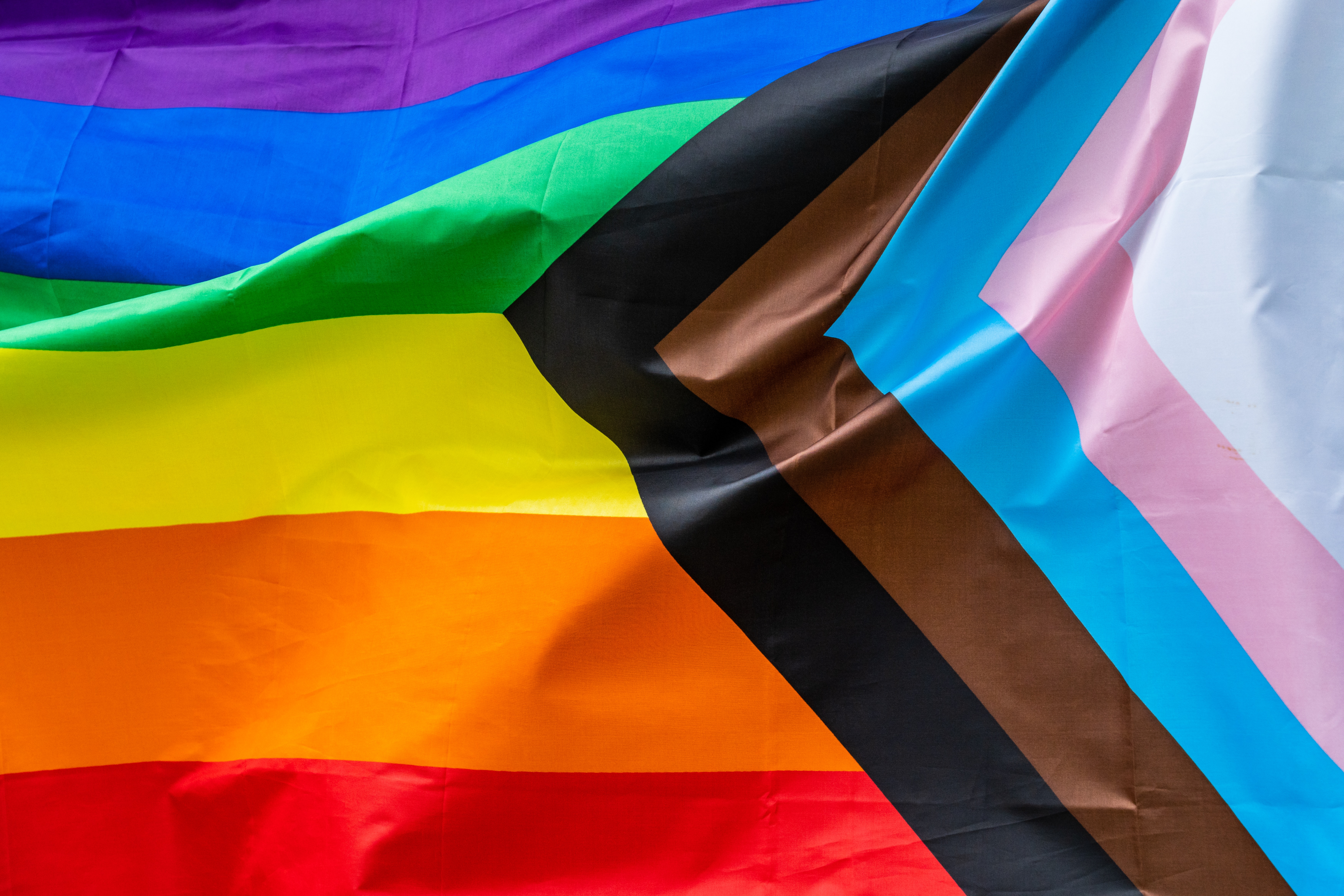 Image shows progressive pride flag blowing in the wind