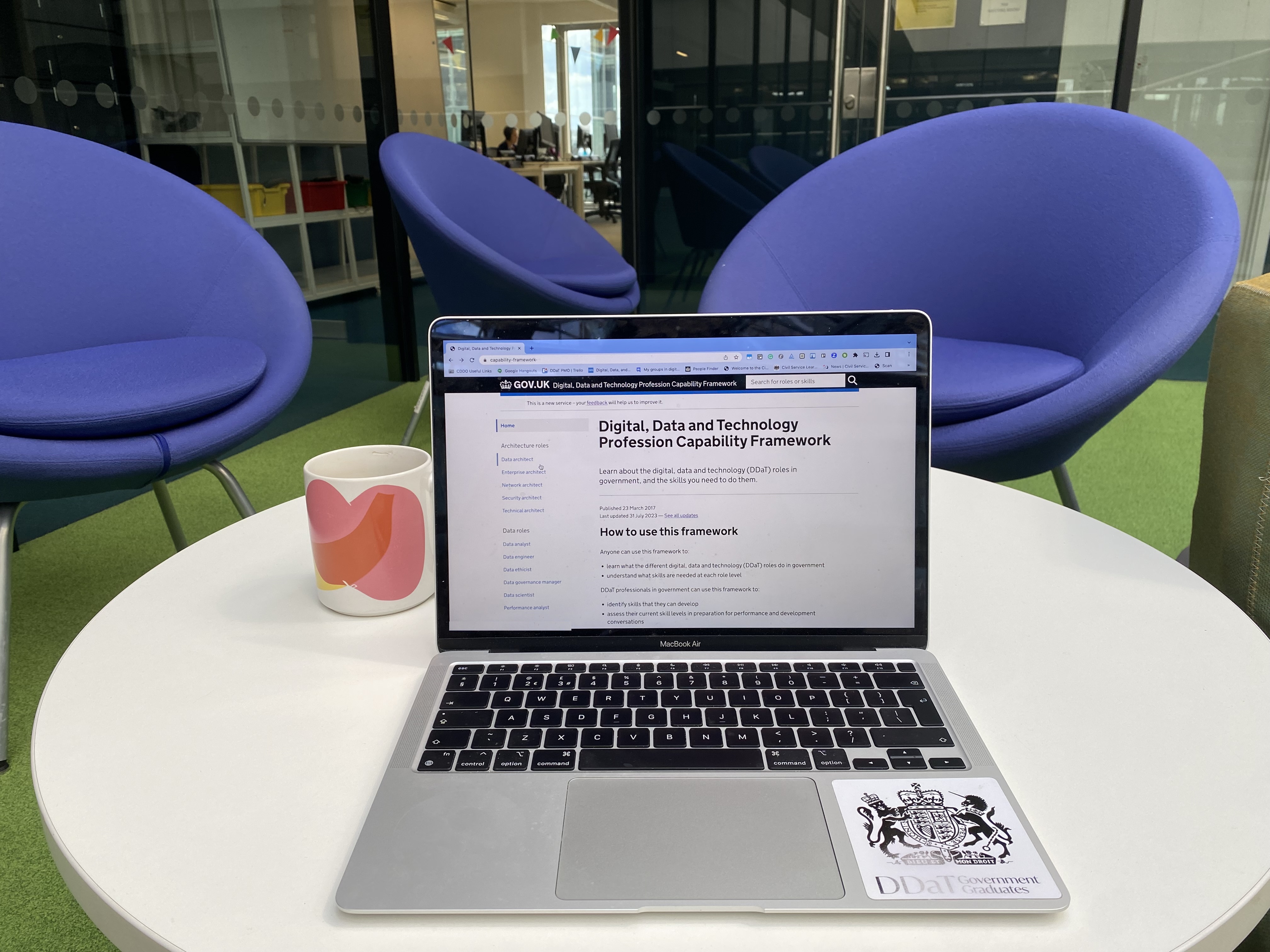 Image shows a laptop on a table, the screen on laptop shows the home page of the Digital, Data and Technology Profession Capability Framework