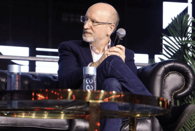 David Knott Government Chief Technology Officer, sitting on a black leather sofa holding a microphone on a panel for ColorinTech.